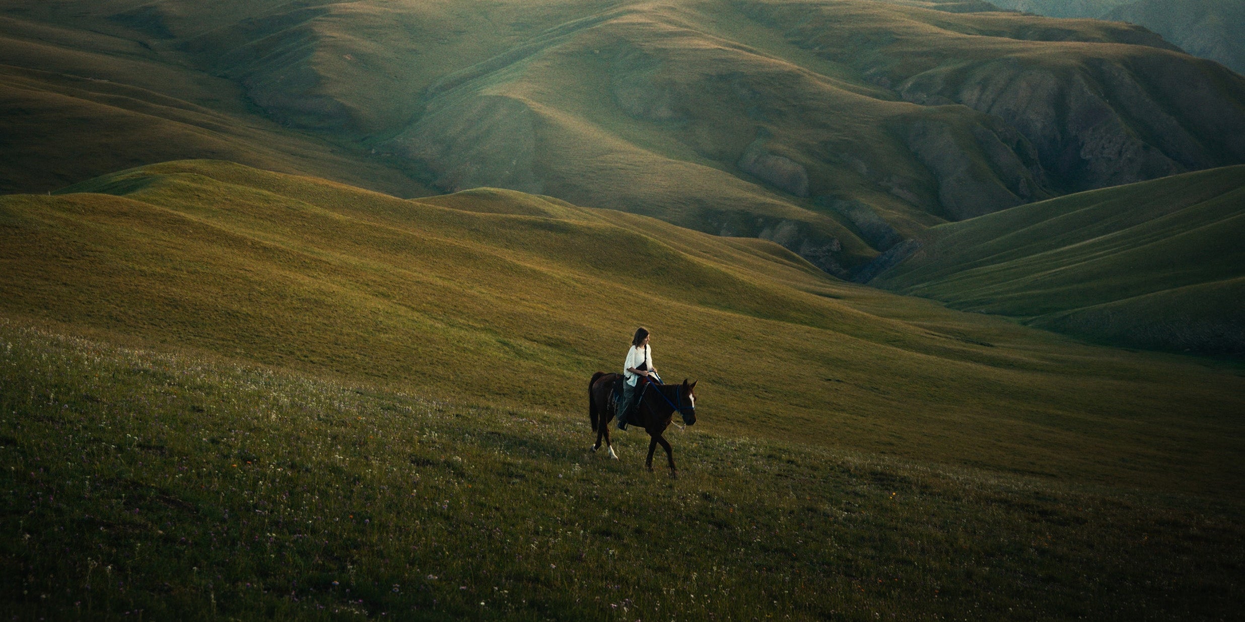 a person riding a horse in the hills of Kyrgyzstan at sunset on a trip with a local guide