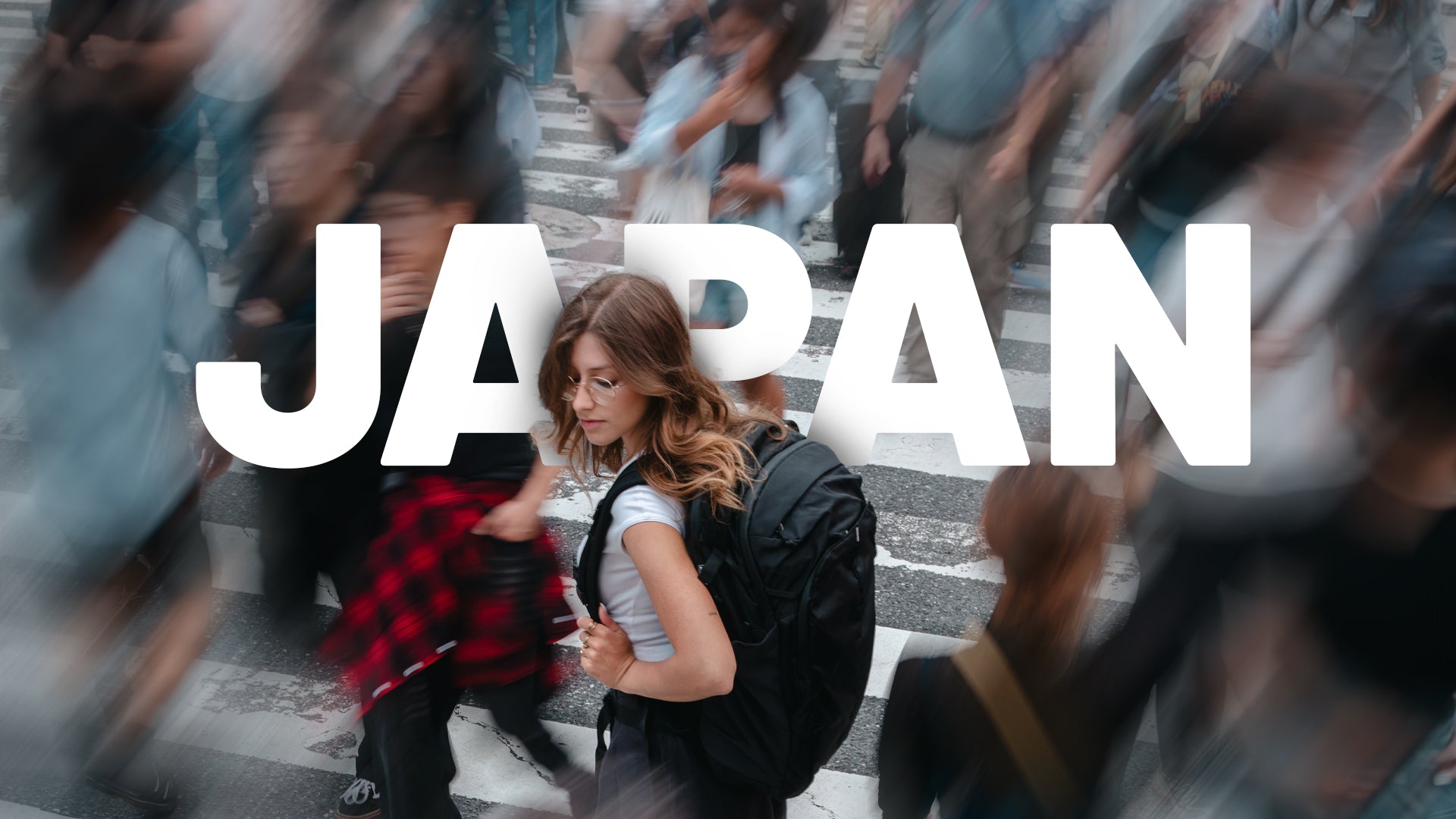 A woman with a black Matador backpack walks across a city crosswalk in a busy urban setting, with large white text reading 'JAPAN' overlaid across the center.