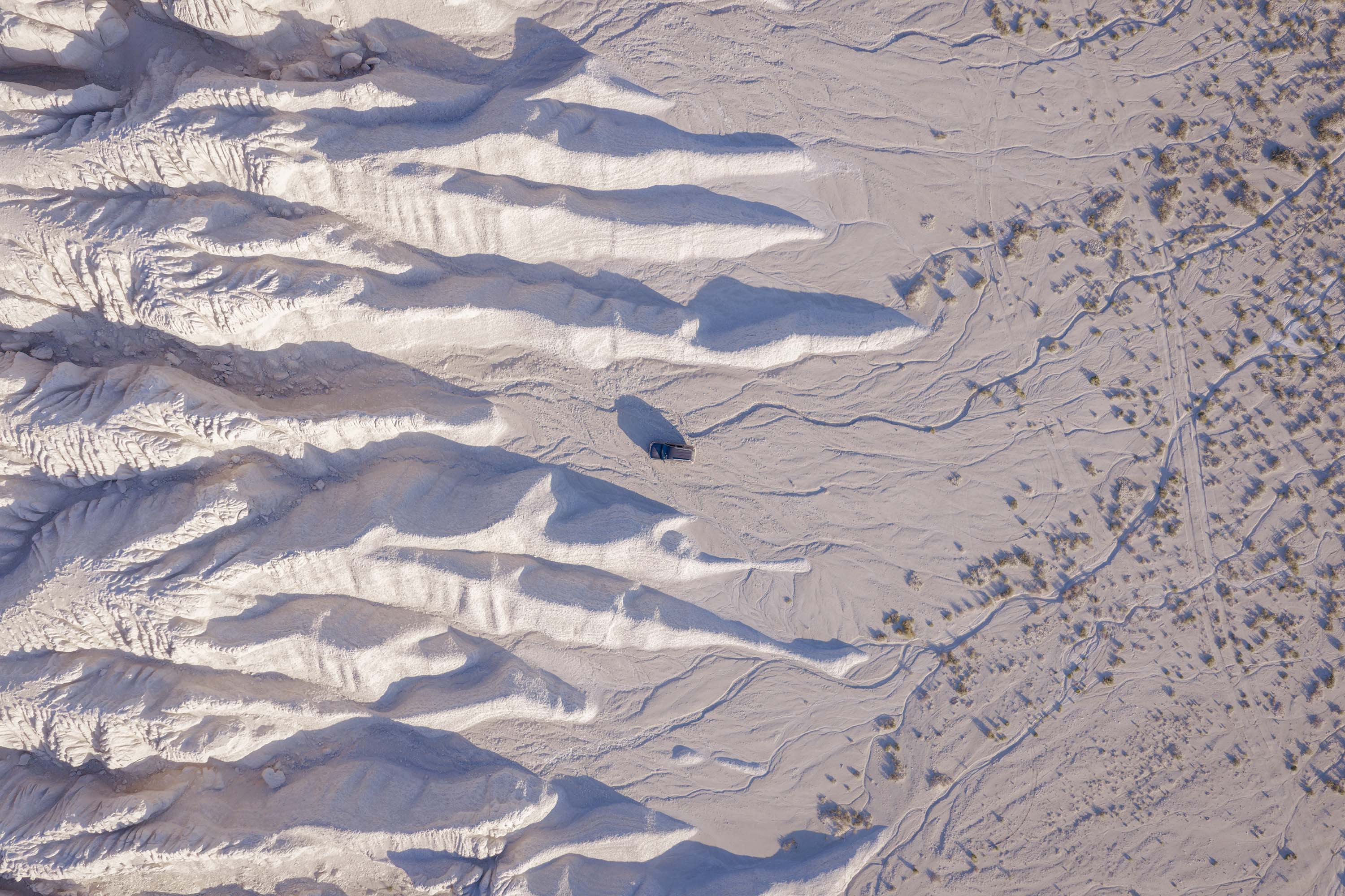 Aerial view of a Tuzbair salt flats with dramatic ridges and shadows, alongside a dry desert area with sparse vegetation.