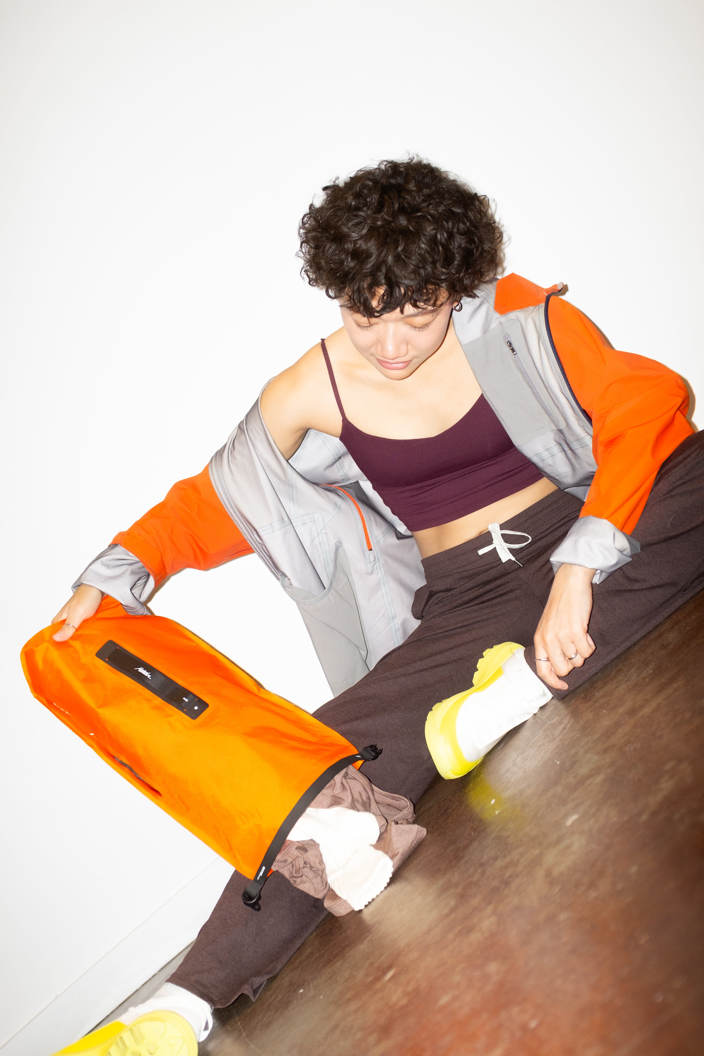 Person holding an orange dry bag and dumping out dry clothes with a white background