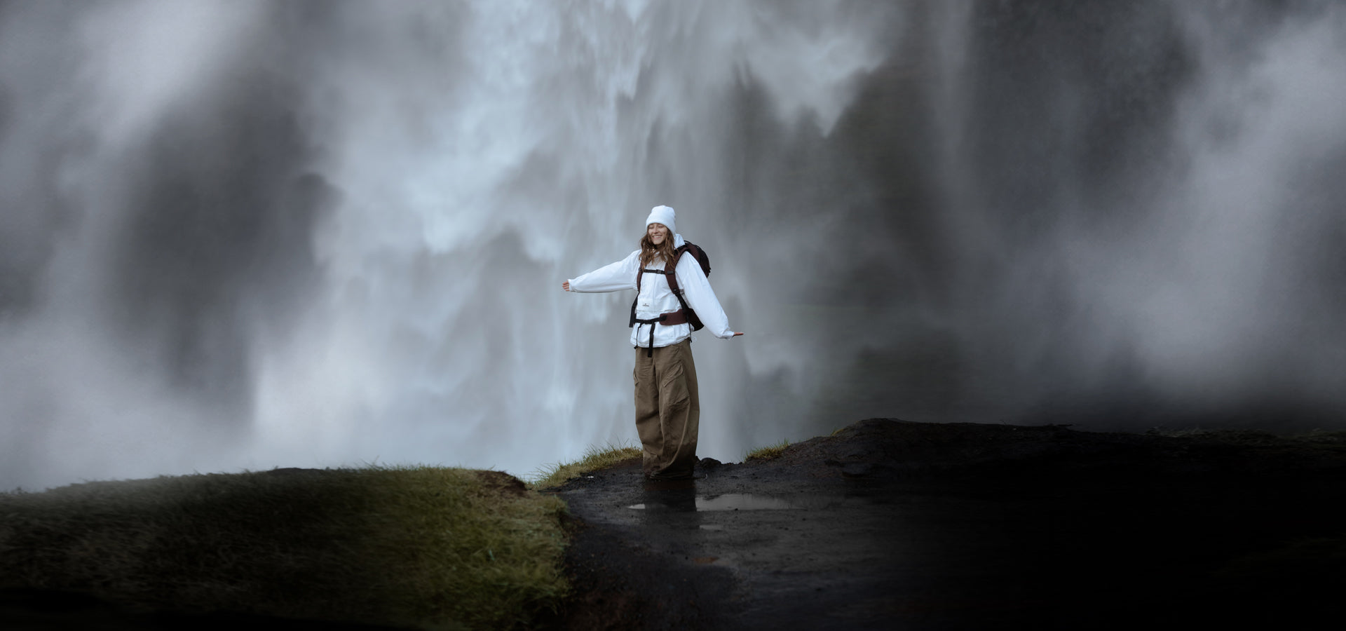 woman in white jacket smiling in front of waterfall