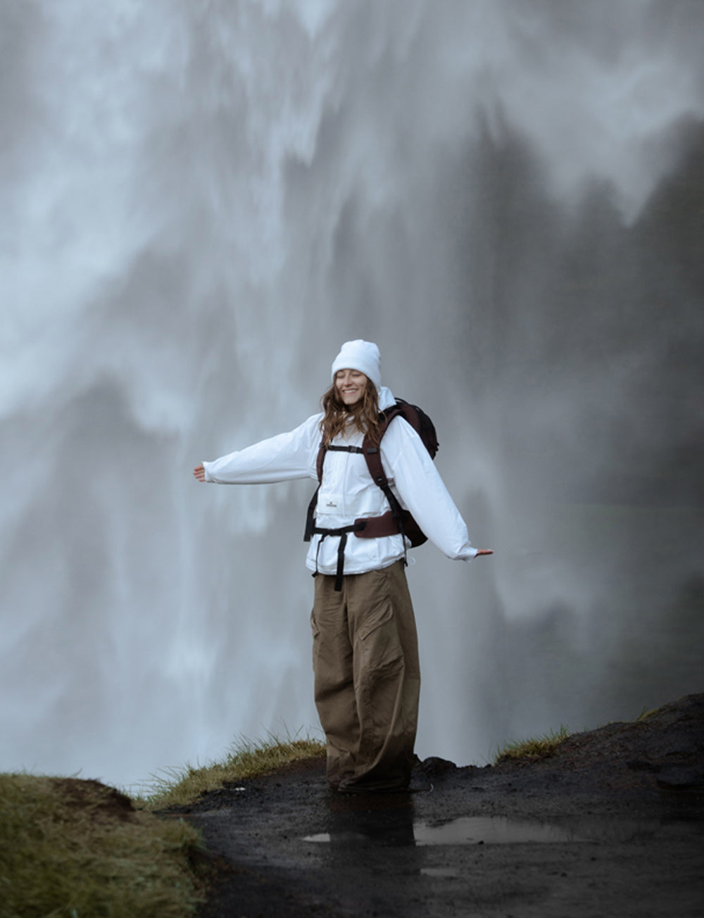woman in white jacket smiling in front of waterfall