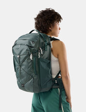 A woman shown from the back wearing a dark green technical backpack, set against a plain light gray studio background.