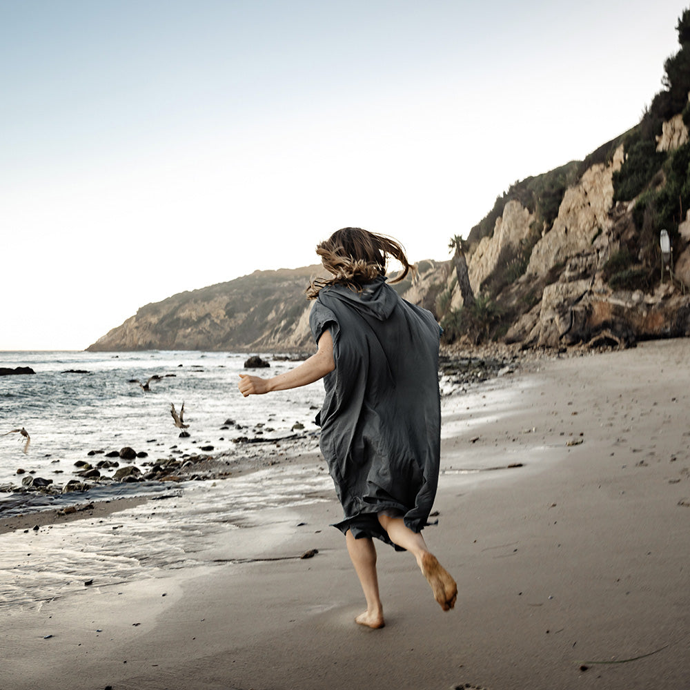 woman wearing gray poncho running on beach