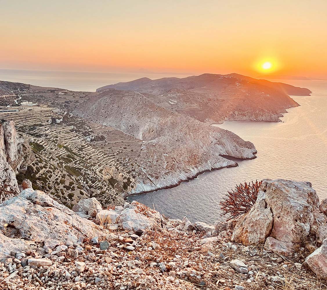 Sunset over a coastal landscape with rocky terrain and a body of water.