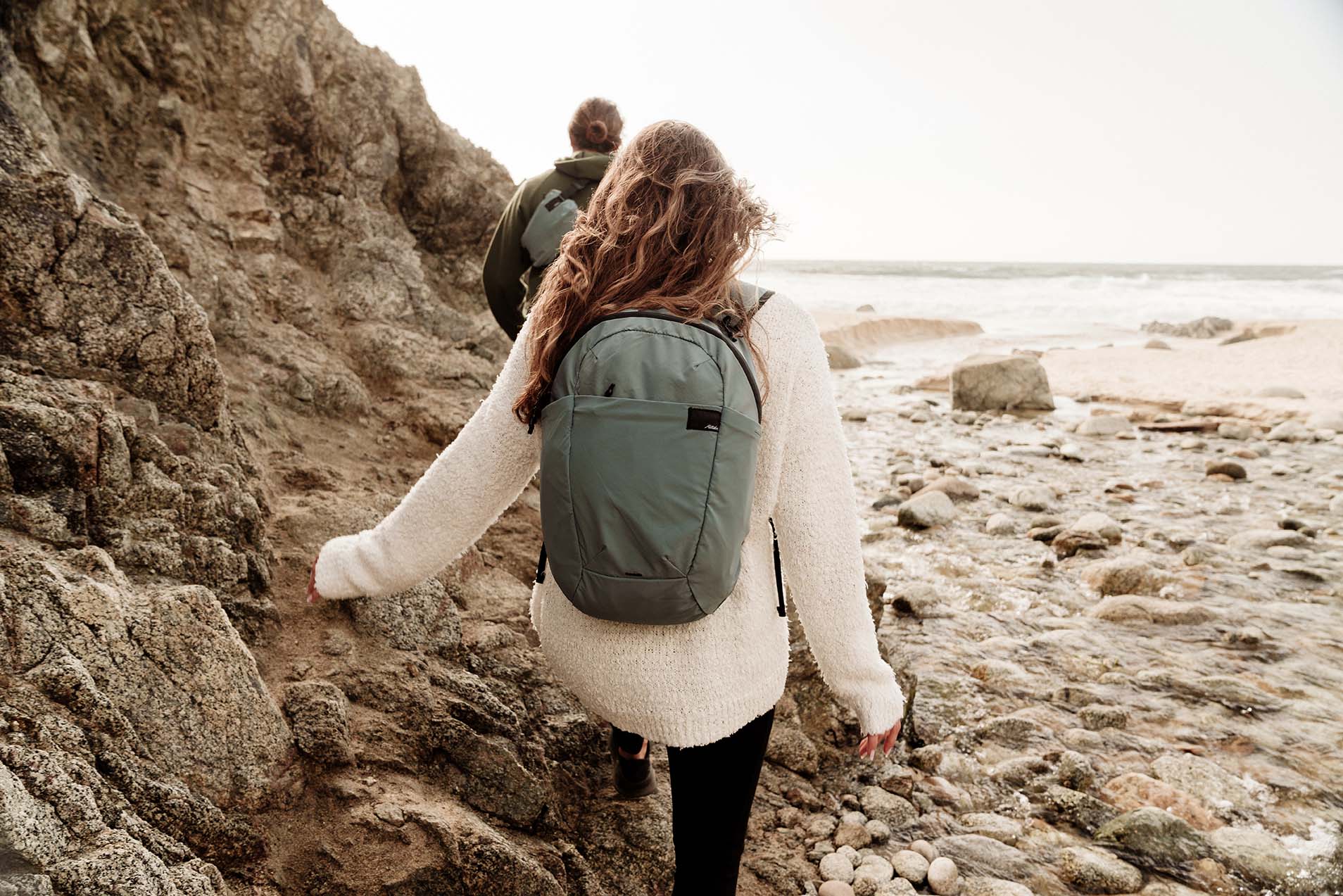 Two people hiking along a rocky coastline with packable backpacks.