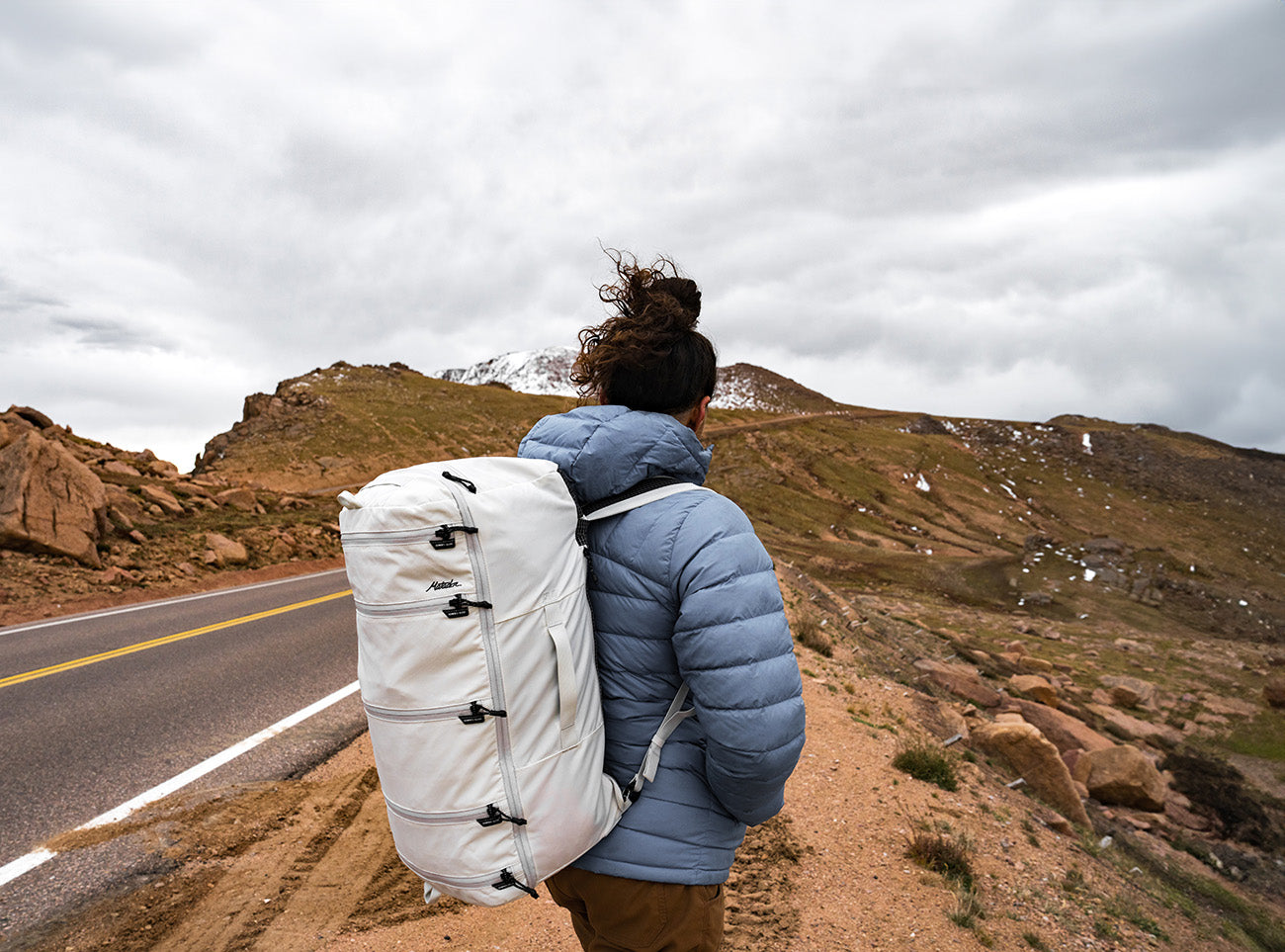 person traveling in the winter with a white backpack next to a road