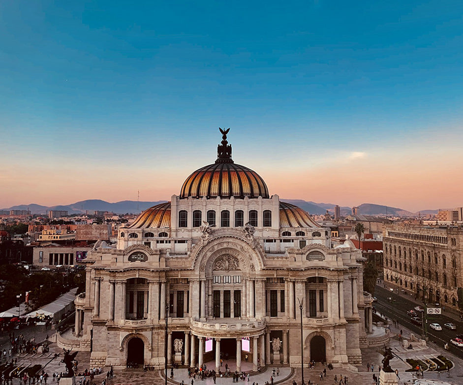 Grand architectural building with a dome at sunset, surrounded by cityscape in Mexico City